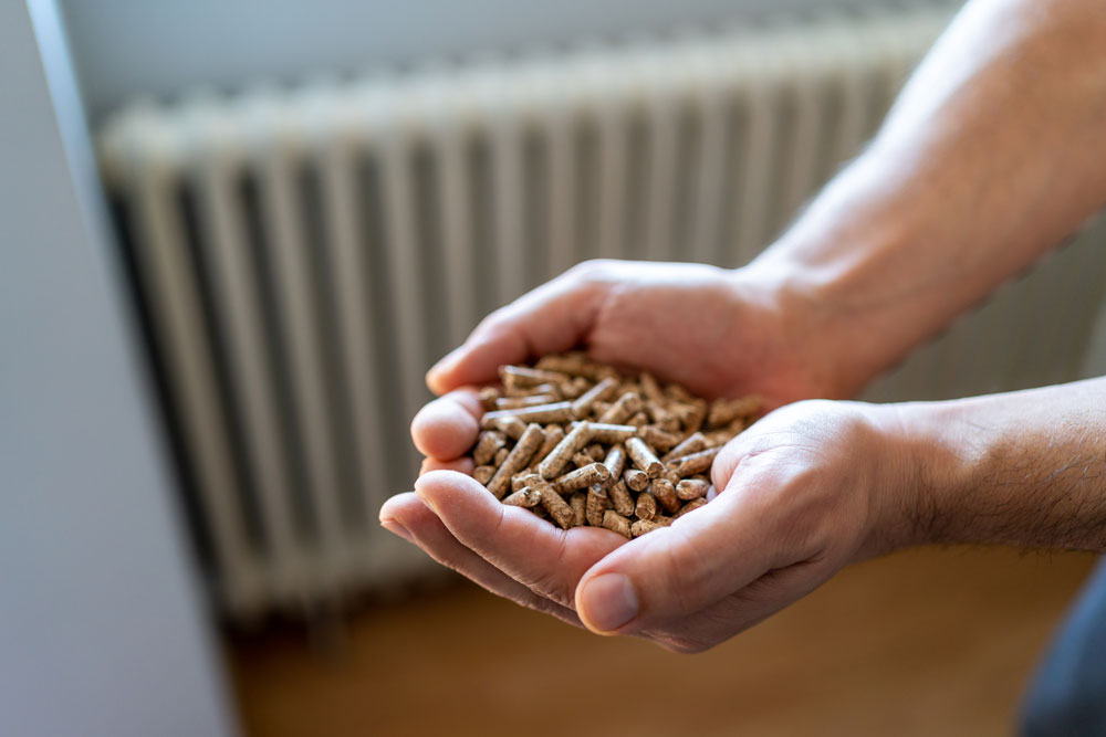 hands holding wood pellets with a heater in the background